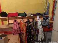 Photo showing assorted ladies scarves draped over a wooden coat rack with five pegs, some scarves hanging and some folded, along with pairs of gloves.