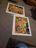 Photo showing both Peter Zonis serigraphs lying on floor, displaying carnival scenes in bold Fauvist style colors and composition.