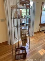 Full view of the tall metal shelving unit with towels and various items displayed on the shelves, including vintage lace and wooden blocks underneath.