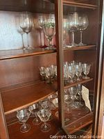 Tall and short assorted crystal stemware glasses displayed in wooden cabinet.