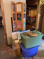 Shows a three-part wooden folding photo screen with attached portrait photographs standing beside bins and other items.