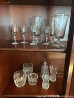 Shelf with multiple pieces of assorted crystal and etched glass drinkware including stemmed glasses and goblets of varying sizes.