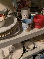 Multiple ceramic mugs, white plates and bowls, a serving bowl with floral pattern visible