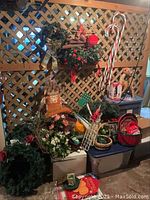 View of Christmas wreaths, stuffed stocking, candy cane decorations, greenery garlands, and the Annalee reindeer figurine alongside assorted holiday decorations stacked on and around plastic storage bins.