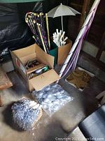 Photo showing multiple batons, a white parasol, a star wand, bags of silver decorations, and a tall maypole with ribbons, all arranged in boxes and standing upright.