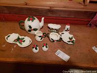Full view of Lefton ceramic Christmas set on wooden surface with teapot, cream, sugar bowl (missing lid), salt and pepper shakers, and four dishes, plus Holt Howard bell.