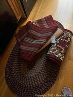 Photo showing the three rugs together, one oval braided rug and two rolled rectangular rugs with distinct patterns