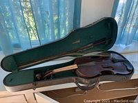 Antique violin inside hard case with bow lying across case lid.