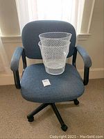 Blue padded fabric office chair with one white metal mesh trash can placed on the seat, showing size and style.