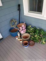 Photo showing various planters in ceramic, clay, and woven baskets, artificial pink flowers and green foliage, wreath, and 3-hook black metal plant stand