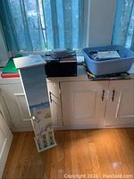 Photo showing assorted items including green vinyl record, CDs stacked, stereo tapes, DVDs in plastic bin, and white standing cabinet