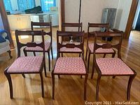 Six vintage mahogany dining chairs with pink upholstered seats arranged in two rows on a polished wood floor.