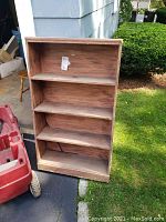 Front view of the solid wood 4-shelf bookcase showing the full frame and shelves outdoors on pavement.