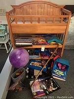 View of the lot with wooden shelf holding games and books, purple exercise ball, walking cane, and containers with Matchbox cars.