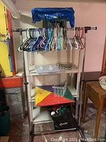 Wide view of the adjustable rolling shelf with hangers on the rod and storage baskets on shelves