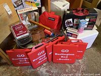 Photo showing red cushioned folding seat cushions with 'Go Burlington Red Devils' text and several boxed items including a BBQ grease cup and wood cutting boards.