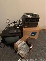 Photo showing small CRT television, DVD player on top, and Poly Cam phone in box along with power cables on floor.
