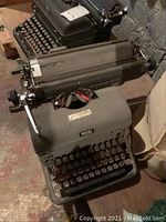 Two vintage manual Royal typewriters placed on the floor. One olive green in front and a black one behind it.