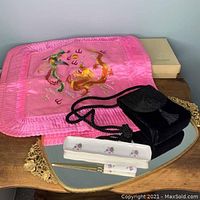 Lot displayed on wooden surface showing the two pink embroidered pillow covers with phoenix and dragon, black velvet corded Lord & Taylor bag, Neiman Marcus porcelain letter opener and pen tray on mirrored Matson tray.