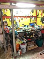 Photo showing workbench surface and items on it including tools, extension cords, rope, buckets, paint cans, and other hardware.