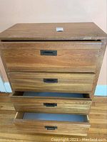 Front and side view of wood bureau showing four drawers with metal recessed handles. One drawer partially open, highlighting good structural condition with minor surface wear on top.