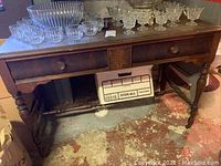 Full view of vintage wooden sofa table with glassware on top, showing turned legs and drawer with knobs.