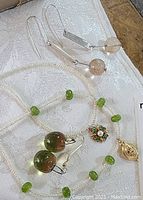 Shows earrings on a white fabric surface with necklace and pendants, highlighting bead colors and earring design