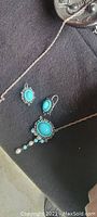 Full view of necklace and earrings on black surface showing turquoise stones and pearl-like dangles.