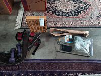 Overview of the lot showing all items on floor and against a wooden rack, including knee brace, hand weights, glass swans, calculator, massager, and hardware pieces