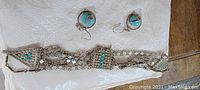 Full view of bracelet and earrings on fabric background showing turquoise stones and decorative metal disks on bracelet and round earrings