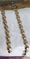 Photo showing the full necklace and bracelet laid out separately on a white fabric, highlighting the spherical gold-tone beads and the links.