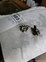 Two sterling silver cufflinks with an abstract design photographed on a white textured fabric, showing front and back sides.