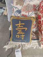 Throw pillows stacked showing blue pillow with gold Chinese character 'Longevity' and floral patterned pillows behind