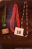 Photo showing two bead necklaces, a green heart pendant necklace, a small wooden box, and a pair of bead hoop earrings.