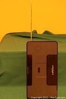 Black rectangular portable speaker system with front grille and extended copper FM antenna against yellow and green background