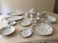 Overall layout of the Blue Garland porcelain dinnerware pieces showing various plates, platters, and serving dishes on a beige tablecloth.