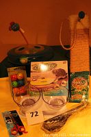 Wide view of the lot showing the cat scratching post, double elevated bowls, catnip bag, grooming scissors, motorized wand toy in box, spherical toy balls, circle track toy, and litter scoop all arranged together.