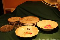 Set of 5 floral china dinner plates stacked with other plates, clear glass bowls, and two peony design serving bowls displayed on a green cloth.