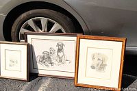 Four framed dog-themed artworks placed on asphalt next to a car, showing the variety of the lot