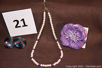 Photo showing all items in the lot: small pearl and purple bead necklace, purple leather flower pin, and plaid earrings.