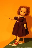 Front view of the Madame Alexander doll in original 1940s dress with porcelain face and arms, showing red shoes and curly hair.