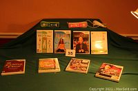 Photo showing two Wii controllers (green and pink with silicone sleeves) and one white nunchuk controller, along with eight Wii game cases arranged in two rows on a green surface against an orange wall.