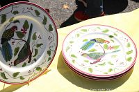 Four colorful charger plates with parrot and floral design resting on a yellow tablecloth, one plate on a stand.