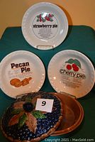 Photo showing three pie plates each with printed recipes for strawberry, cherry, and pecan pies, along with the lidded blueberry-themed pie plate closed.