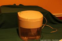 Front and top view of the Royal MD100 shredder showing the beige upper housing and clear wastebasket with a power cord extending from the back.