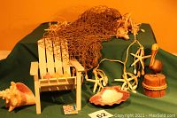 Photo showing garnished small wooden beach chair, fishnet, starfish and shell garland, two large seashells, pelican knick-knack, and pastel votive candles