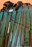 Golf clubs laid out on a green surface with headcovers visible. Shows a mix of irons and woods with metal shafts and various grip styles.