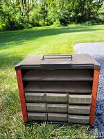 Front view of metal toolbox showing two upper shelves and nine plastic drawers below with rusty metal and faded paint.