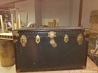 Front view of vintage travel trunk showing multiple brass locks and central latch with leather strap.