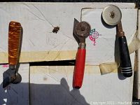 Three wallpapering tools with cutting wheels displayed on a cardboard surface in natural light.
